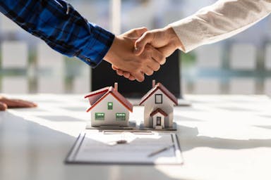 A handshake over models of two houses. An agreement has been reached about the customer's mortgage.