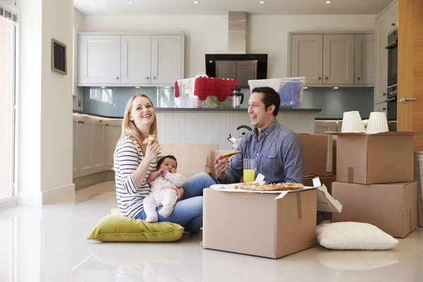A mother, father and baby looking delighted as they eat pizza in the kitchen of their new home.