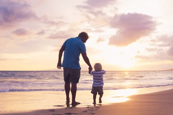 A grandfather takes his son for a walk on a beautiful beach at sunset.